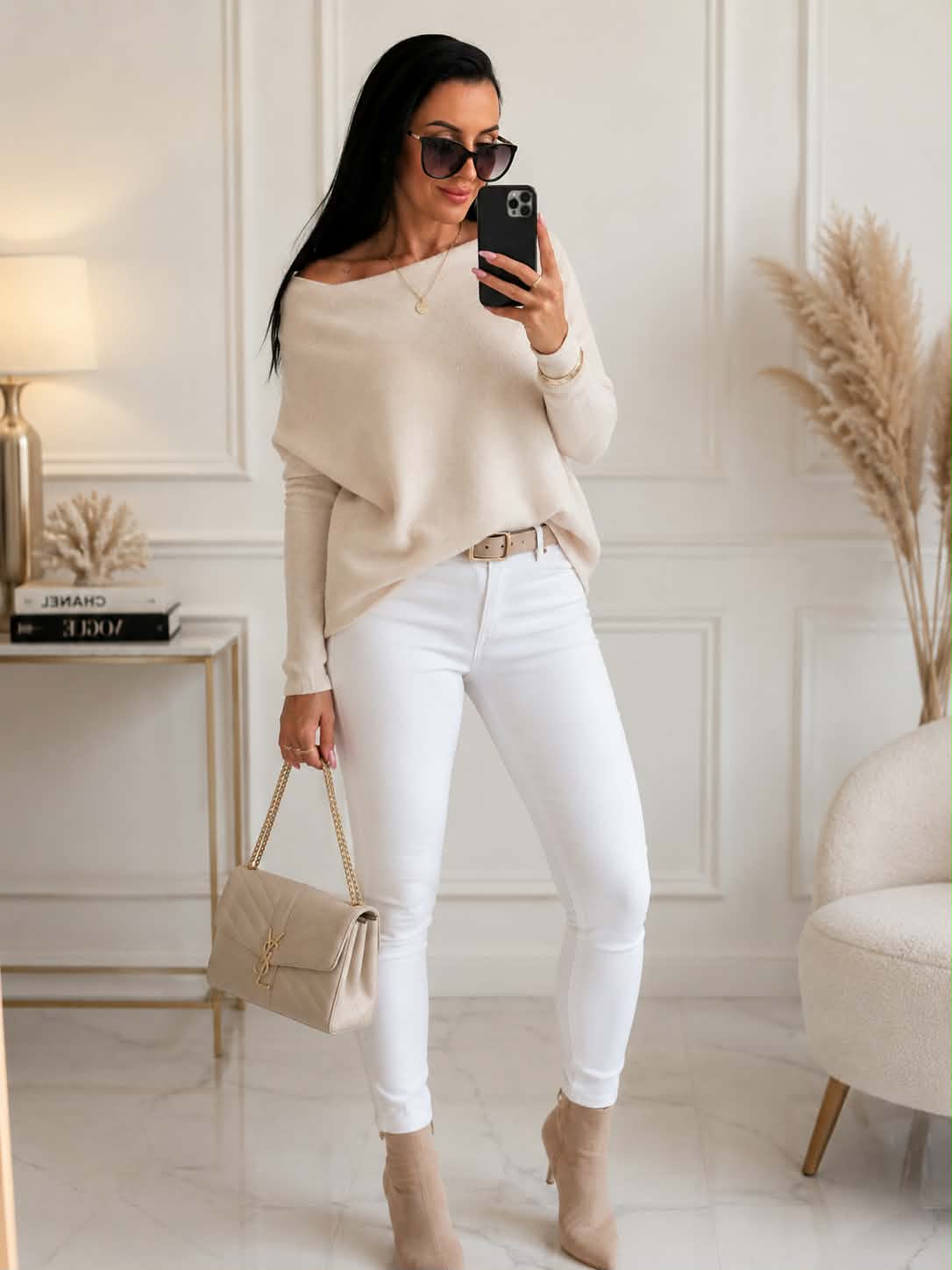 Elegancki damski sweter kaszmirowy oversize w kolorze ecru z dekoltem typu łódka, zestawiony z białymi spodniami i beżową torebką – stylizacja idealna na co dzień i do pracy.