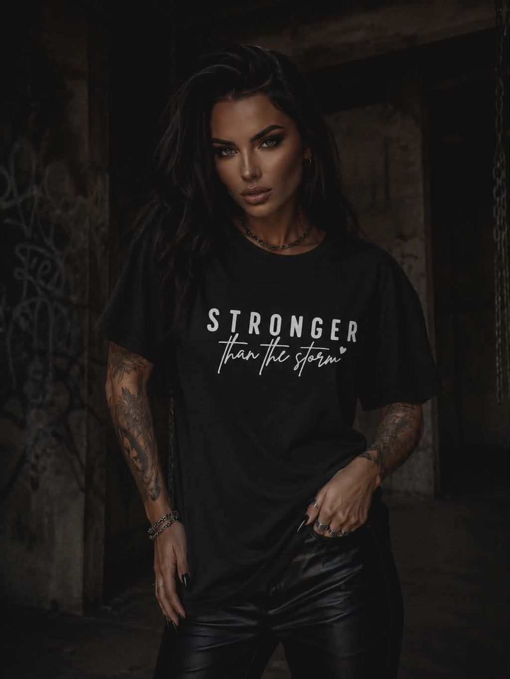 Kobieta prezentująca czarny t-shirt damski Stronger Than The Storm z białym nadrukiem, zestawiony z czarnymi spodniami w rockowym stylu.