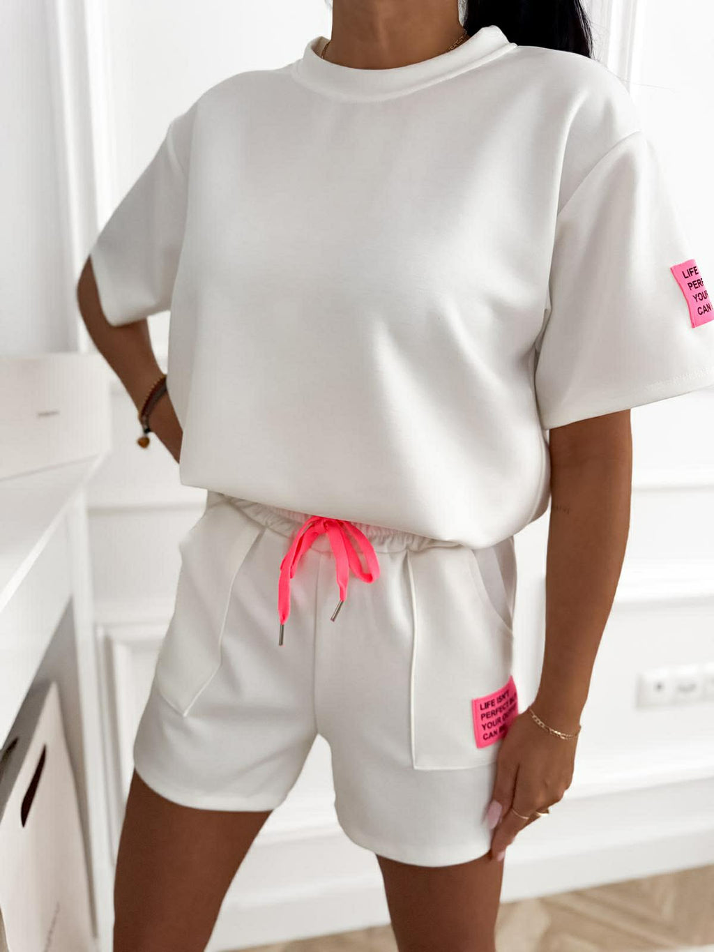 Biały damski komplet sportowy premium z neonowymi detalami, wygodnymi szortami i luźną koszulką idealny na lato i codzienny casual look.