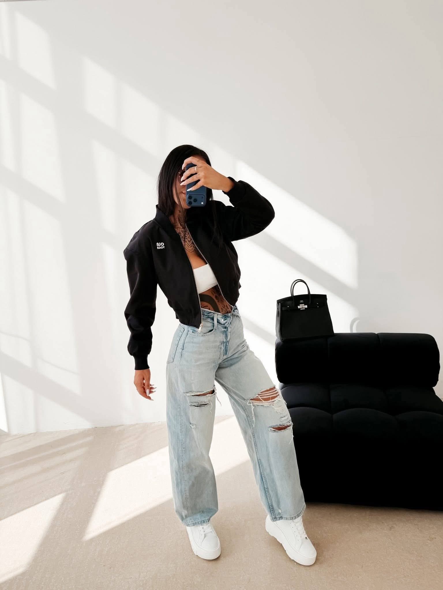Stylizacja z czarną bomberką damską Ola Voga Masti, krótka kurtka streetwear, jeansy z przetarciami i sneakersy, modny look casual