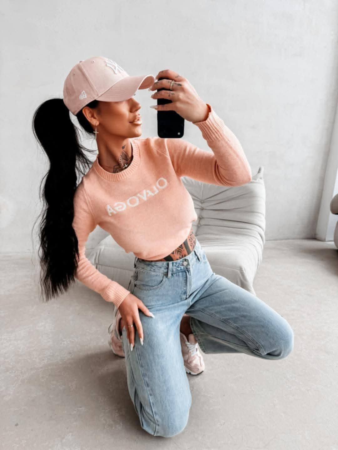 Dopasowany sweter damski OLAVOGA w kolorze łososiowym, długi rękaw, styl casual, modelka w jeansach i czapce, look streetwear premium