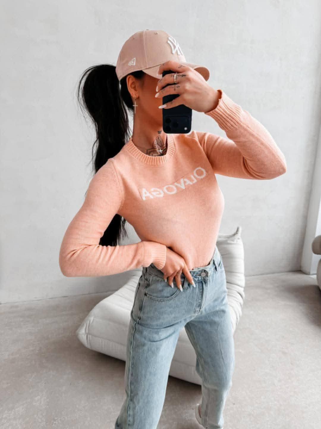 Dopasowany sweter damski OLAVOGA w kolorze łososiowym, długi rękaw, casualowy styl, modelka w jeansach i czapce, nowoczesny look streetwear